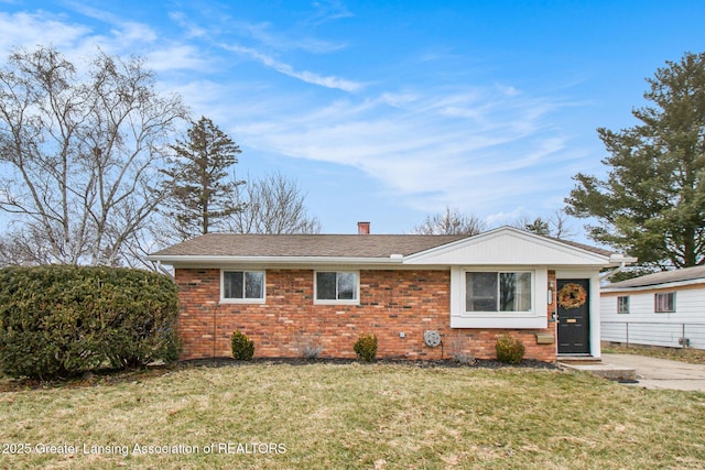 view of front facade featuring brick siding, a chimney, a front yard, and roof with shingles