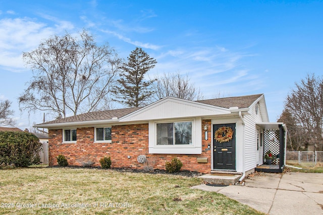 view of front of property with a front yard, fence, driveway, a shingled roof, and brick siding