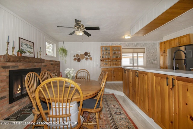 dining room featuring a brick fireplace, a ceiling fan, and light wood-type flooring