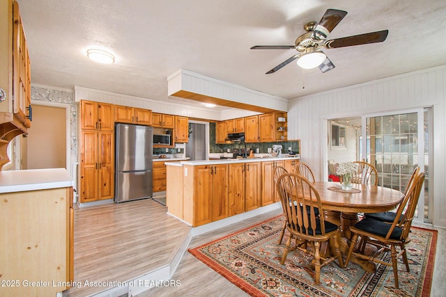 dining room with light wood-style floors, ornamental molding, a ceiling fan, and a textured ceiling