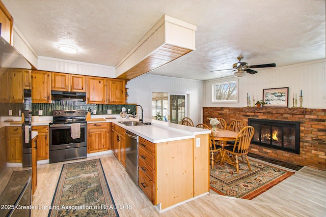 kitchen featuring a sink, under cabinet range hood, appliances with stainless steel finishes, a peninsula, and a fireplace