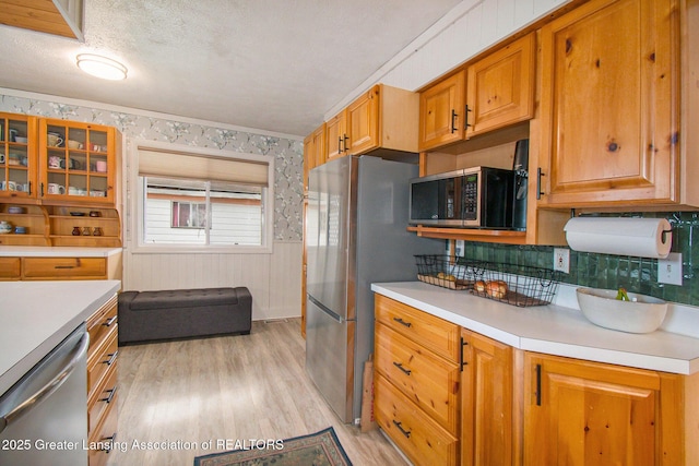 kitchen featuring wallpapered walls, a textured ceiling, appliances with stainless steel finishes, light wood finished floors, and light countertops