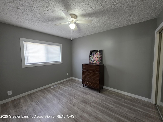 unfurnished bedroom with a ceiling fan, visible vents, wood finished floors, baseboards, and a textured ceiling