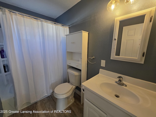 bathroom featuring a shower with curtain, toilet, wood finished floors, vanity, and a textured wall