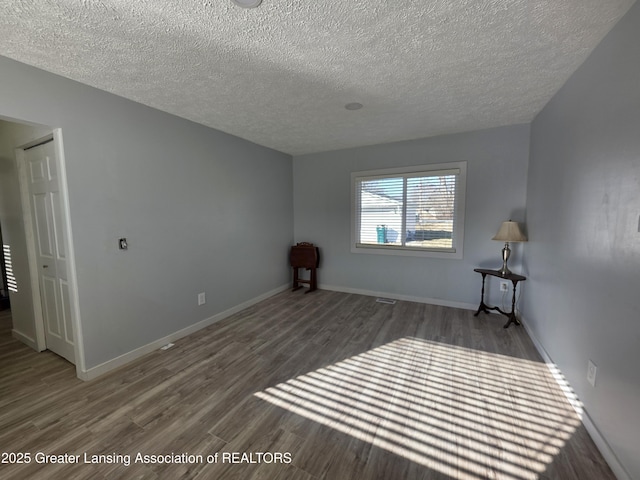 spare room featuring baseboards, a textured ceiling, and wood finished floors