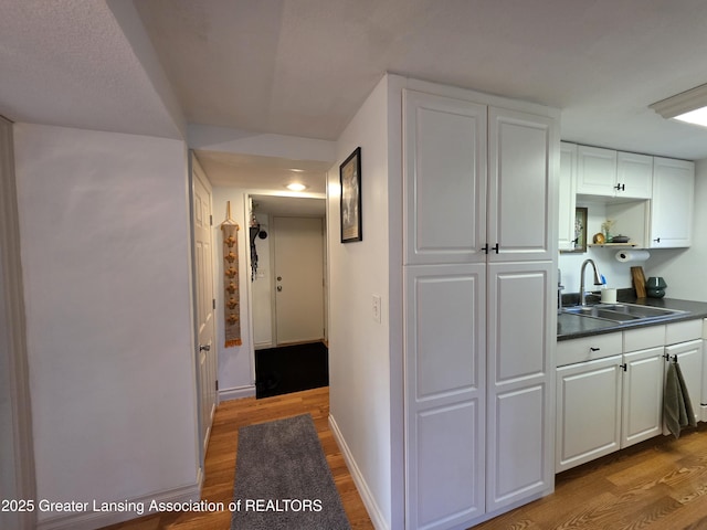 hallway with baseboards, light wood-type flooring, and a sink