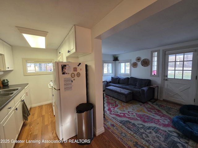 kitchen featuring light wood-style flooring, freestanding refrigerator, a sink, white cabinetry, and open floor plan