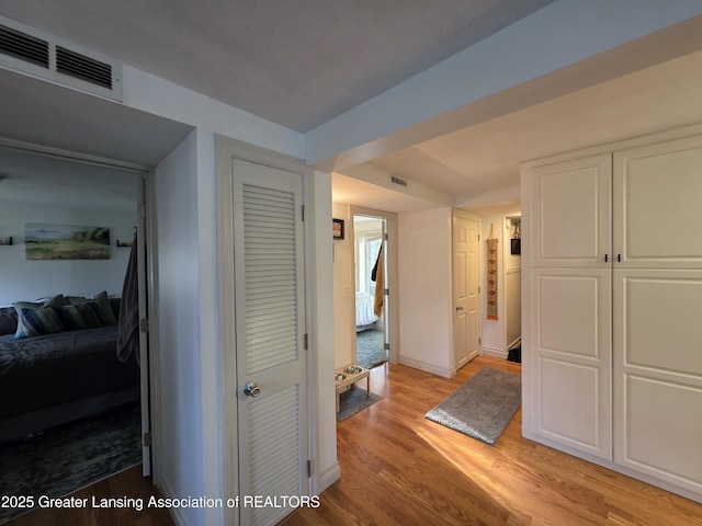 hall featuring light wood-type flooring, visible vents, and baseboards