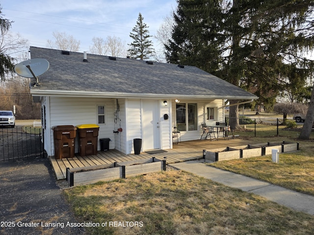 ranch-style home featuring a wooden deck, a shingled roof, a front lawn, and fence