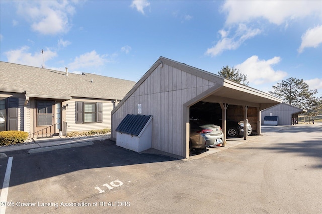 exterior space with covered and uncovered parking, an outdoor structure, and a shingled roof