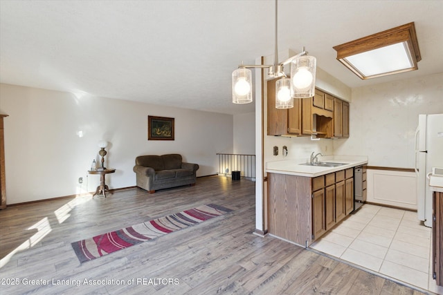 kitchen featuring open floor plan, light countertops, brown cabinets, freestanding refrigerator, and a sink