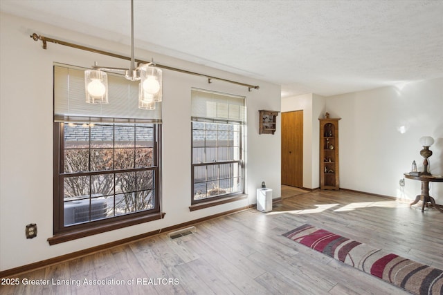 unfurnished dining area featuring visible vents, a textured ceiling, baseboards, and wood finished floors