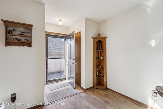 entrance foyer featuring baseboards, light wood finished floors, and a textured ceiling