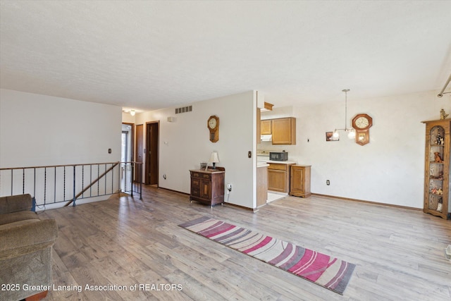 unfurnished living room with visible vents, baseboards, a textured ceiling, and light wood-style flooring