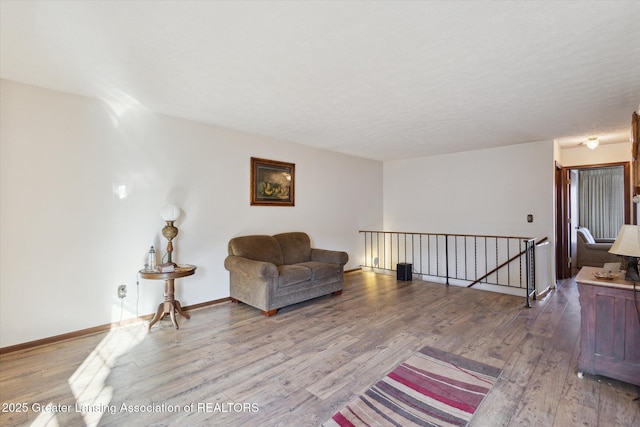 sitting room featuring an upstairs landing, a textured ceiling, baseboards, and wood finished floors