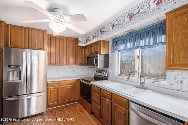 kitchen featuring light wood finished floors, light countertops, appliances with stainless steel finishes, brown cabinetry, and a sink