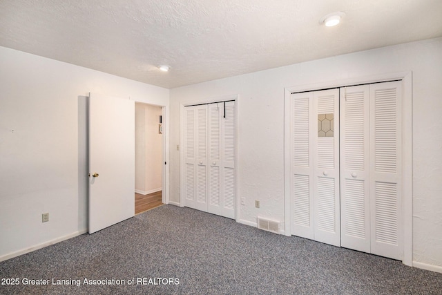 unfurnished bedroom featuring visible vents, two closets, baseboards, carpet floors, and a textured ceiling