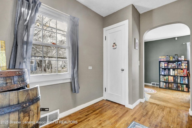 entryway featuring baseboards, arched walkways, visible vents, and wood finished floors