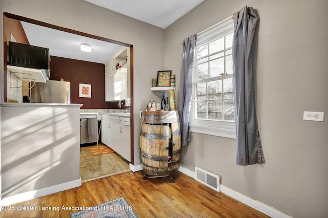 kitchen with visible vents, light wood finished floors, a sink, stainless steel appliances, and white cabinets