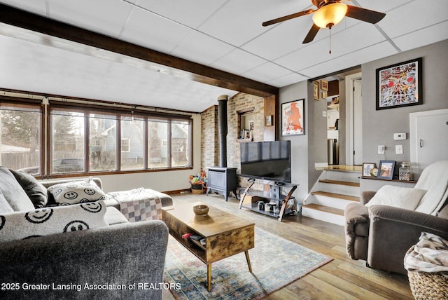 living area with wood finished floors, a wood stove, a paneled ceiling, and beamed ceiling