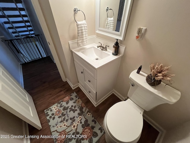 half bathroom featuring vanity, toilet, wood finished floors, and baseboards