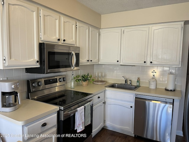 kitchen with appliances with stainless steel finishes, white cabinetry, light countertops, and a sink