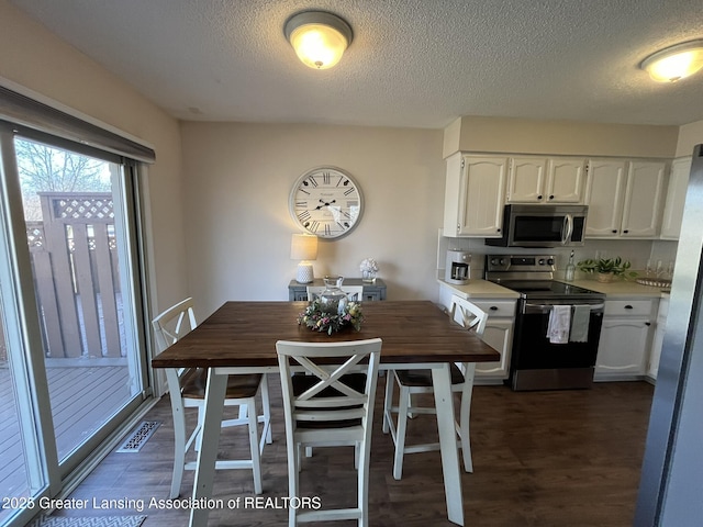 dining space with visible vents, a textured ceiling, and dark wood finished floors