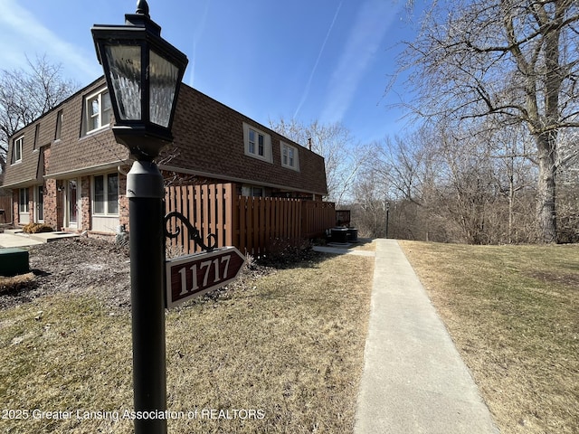 view of side of property featuring a yard, fence, brick siding, and a shingled roof