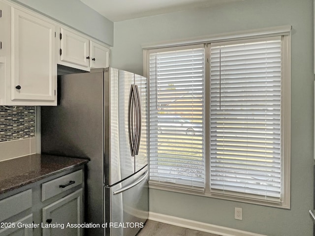 kitchen featuring decorative backsplash, dark stone countertops, white cabinetry, and freestanding refrigerator