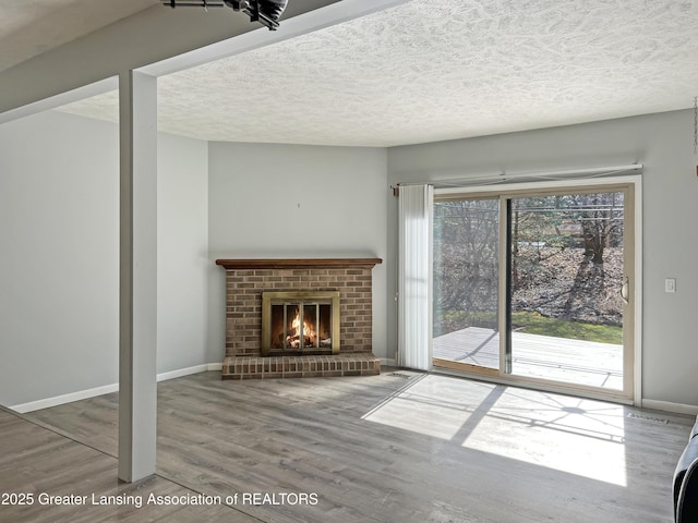 unfurnished living room featuring a fireplace, a textured ceiling, baseboards, and wood finished floors