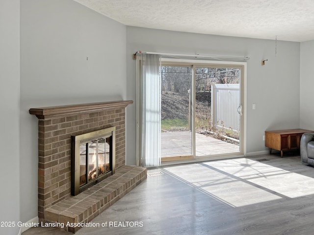 living area with baseboards, a textured ceiling, a brick fireplace, and wood finished floors