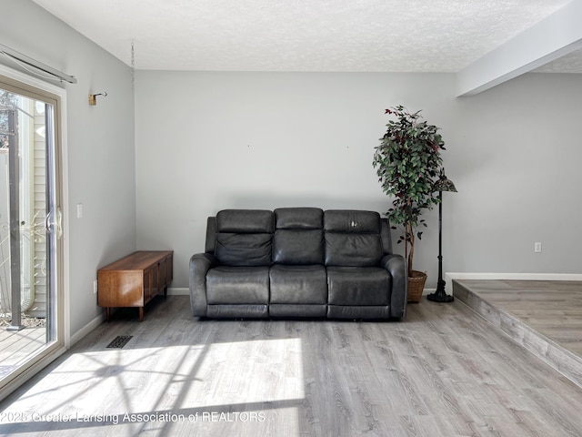 living area featuring a wealth of natural light, baseboards, a textured ceiling, and wood finished floors