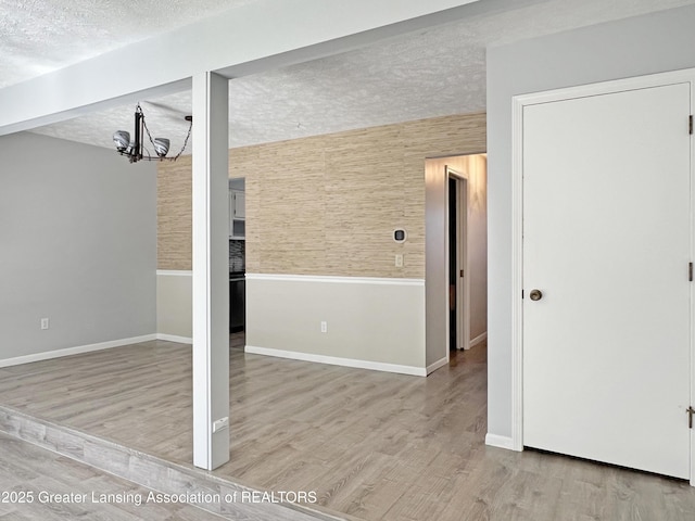 interior space with a chandelier, a textured ceiling, baseboards, and wood finished floors