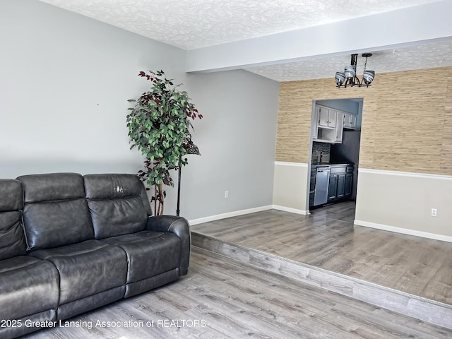 living area featuring an inviting chandelier, wood finished floors, baseboards, and a textured ceiling