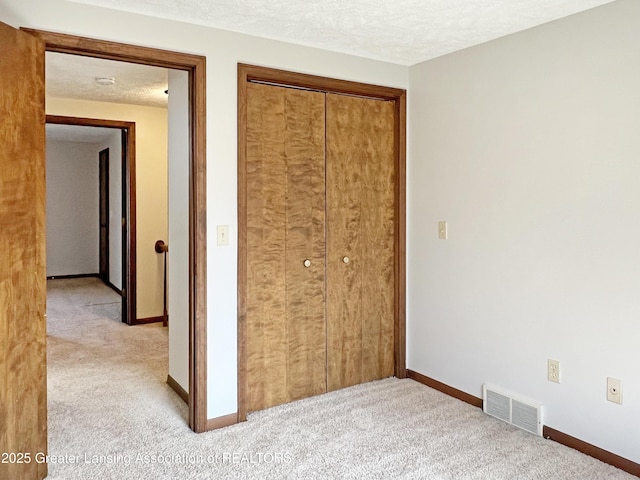 unfurnished bedroom with visible vents, baseboards, light colored carpet, a closet, and a textured ceiling