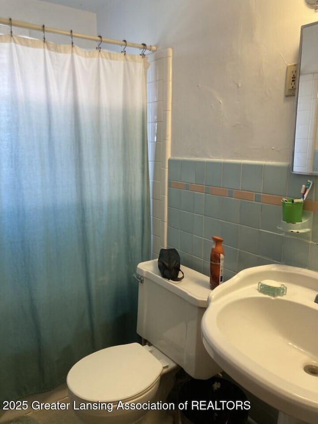 bathroom with a shower with shower curtain, tile walls, toilet, and a sink