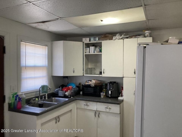 kitchen featuring dark countertops, a drop ceiling, freestanding refrigerator, and a sink