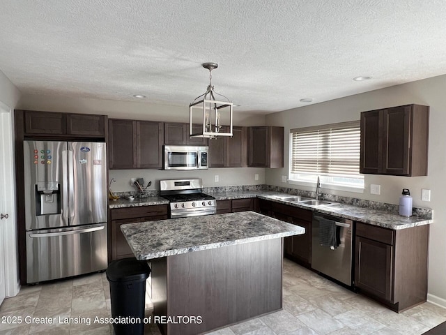 kitchen featuring light stone counters, a kitchen island, a sink, stainless steel appliances, and dark brown cabinetry