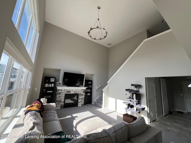 living room with stairway, a high ceiling, a stone fireplace, and a notable chandelier