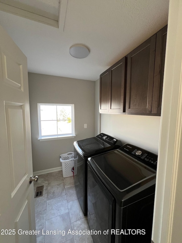 clothes washing area featuring separate washer and dryer, cabinet space, visible vents, and baseboards