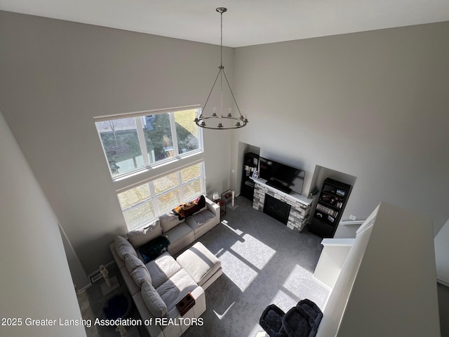 living area with a notable chandelier, carpet, a stone fireplace, and a towering ceiling