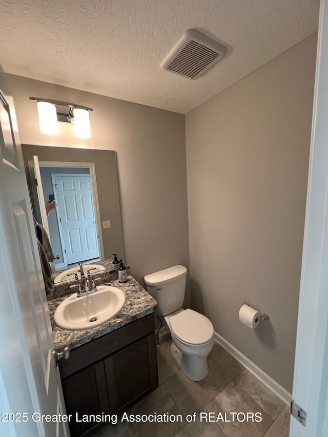 half bathroom featuring visible vents, toilet, vanity, and a textured ceiling