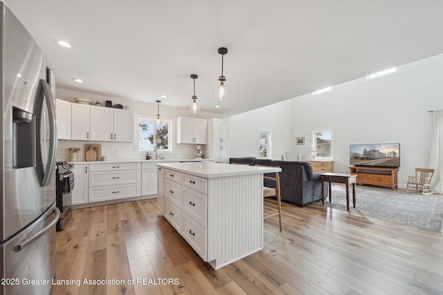 kitchen featuring open floor plan, a breakfast bar, light countertops, light wood-style flooring, and stainless steel appliances