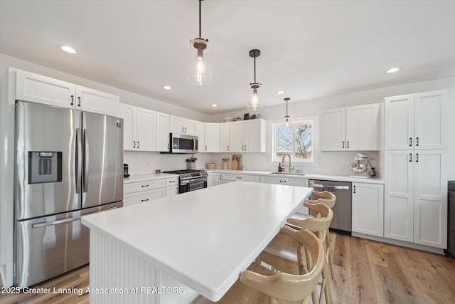 kitchen featuring a kitchen island, light wood-style floors, white cabinets, stainless steel appliances, and a sink