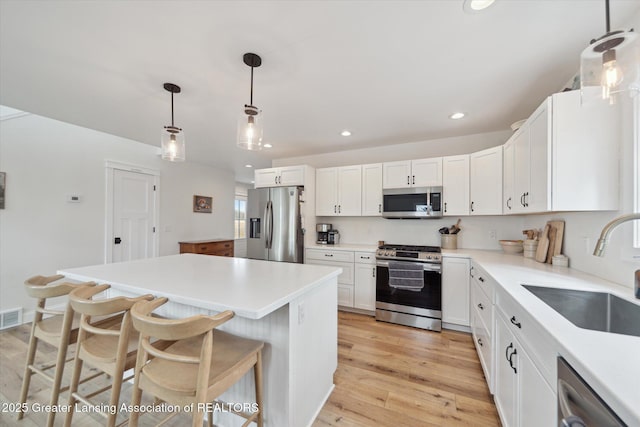 kitchen featuring a breakfast bar area, a sink, stainless steel appliances, white cabinetry, and light wood-type flooring