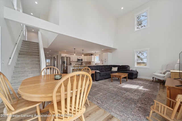 dining area featuring plenty of natural light, stairs, light wood-type flooring, and a towering ceiling