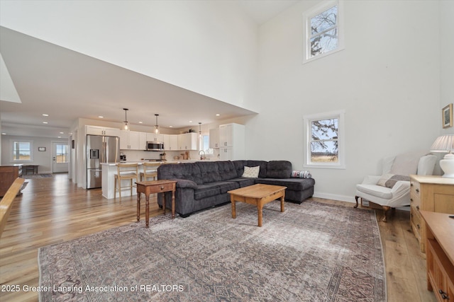 living room with recessed lighting, light wood-type flooring, baseboards, and a towering ceiling