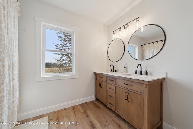 full bath featuring double vanity, wood finished floors, baseboards, and a sink