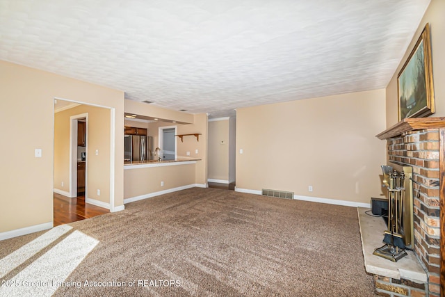 unfurnished living room featuring visible vents, a textured ceiling, baseboards, and carpet floors