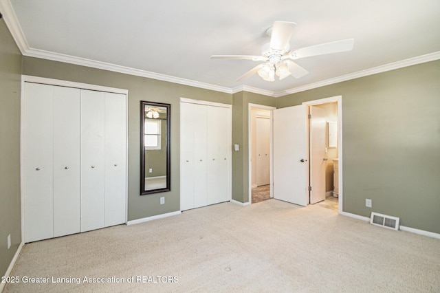 unfurnished bedroom featuring visible vents, two closets, carpet, and ornamental molding